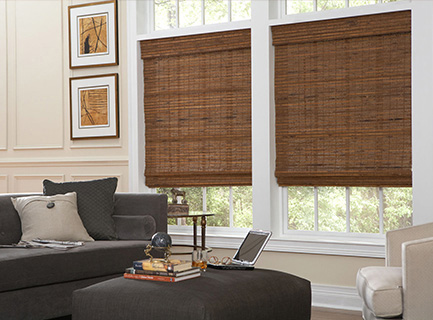 Room scene depicting two cordless, oak woven wood shades in the living area of a house